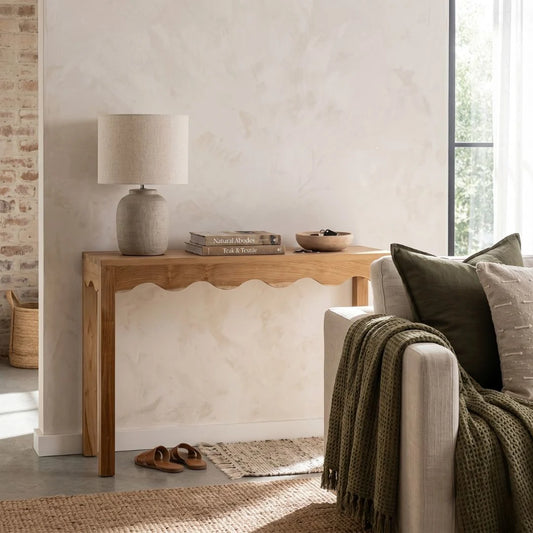 Living room with wooden console table, lamp, and sofa with green blanket and pillows.