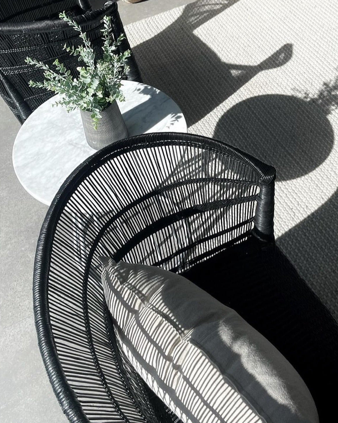 Black wicker chair and table with a plant on a concrete patio