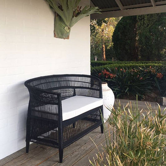 Black wicker chair with white cushion on a wooden deck with plants and garden in the background