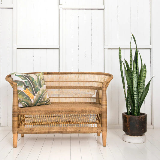 Wicker chair with a tropical pillow and a potted plant on a white wooden floor.