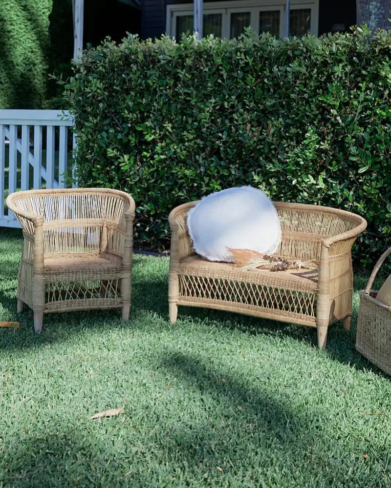 Wicker outdoor furniture set on a grassy area with a hedge in the background