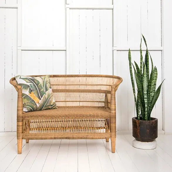 Wicker bench with a decorative pillow and a potted plant against a white wall.