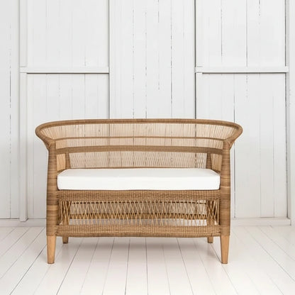 Wicker chair with white cushion next to a potted plant on a white wooden floor.