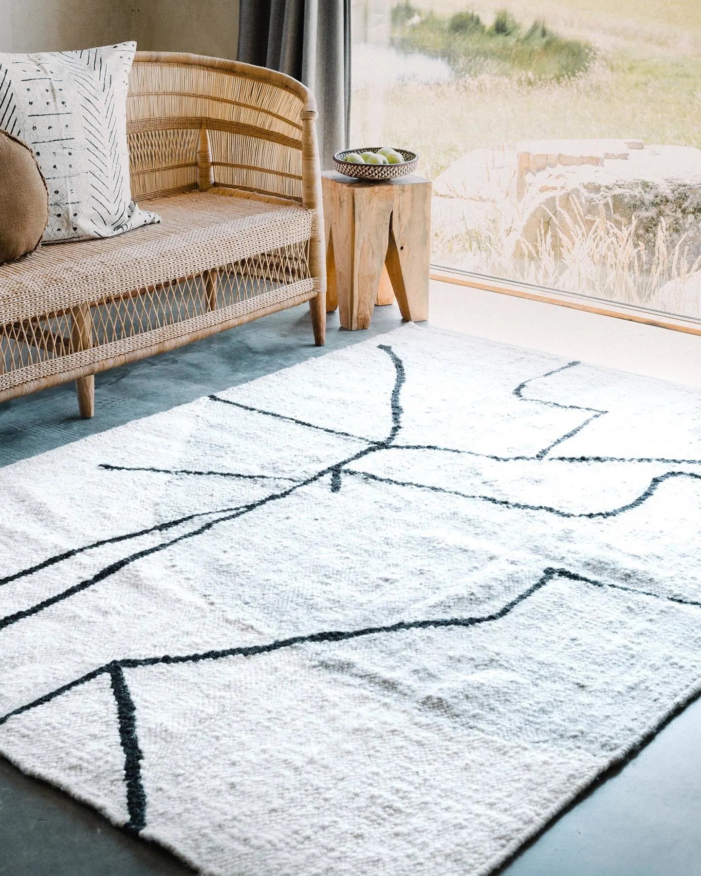 Living room with a wicker sofa, wooden side table, and a patterned rug.