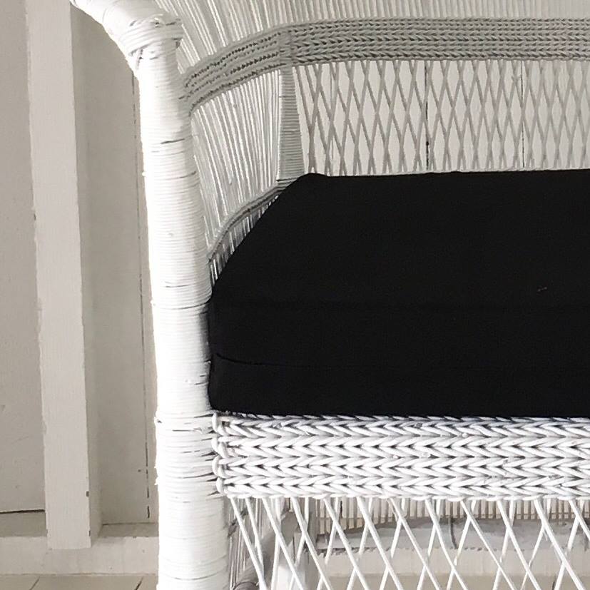 White wicker chair with a black cushion against a white wall