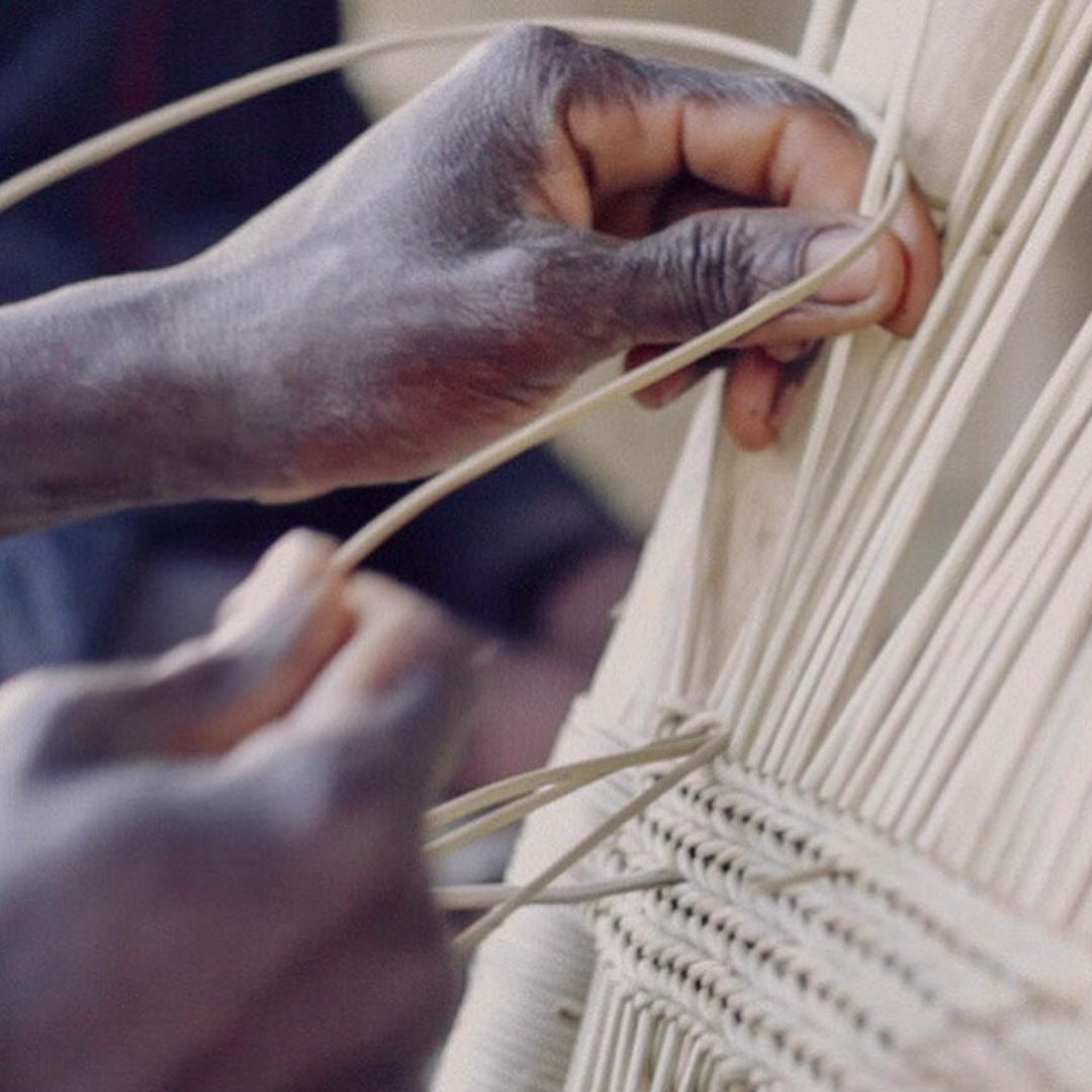 Close-up of hands weaving a beige macrame wall hanging.