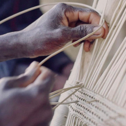 Close-up of hands weaving a beige macrame wall hanging.