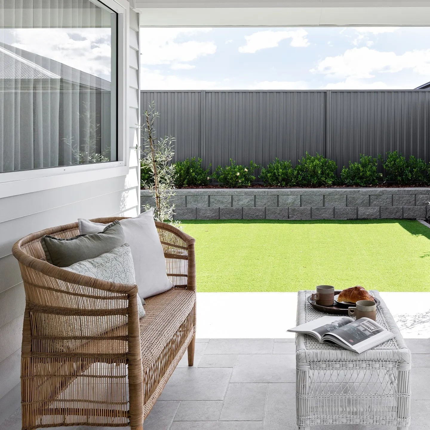 Outdoor patio with wicker bench, coffee table, and view of garden