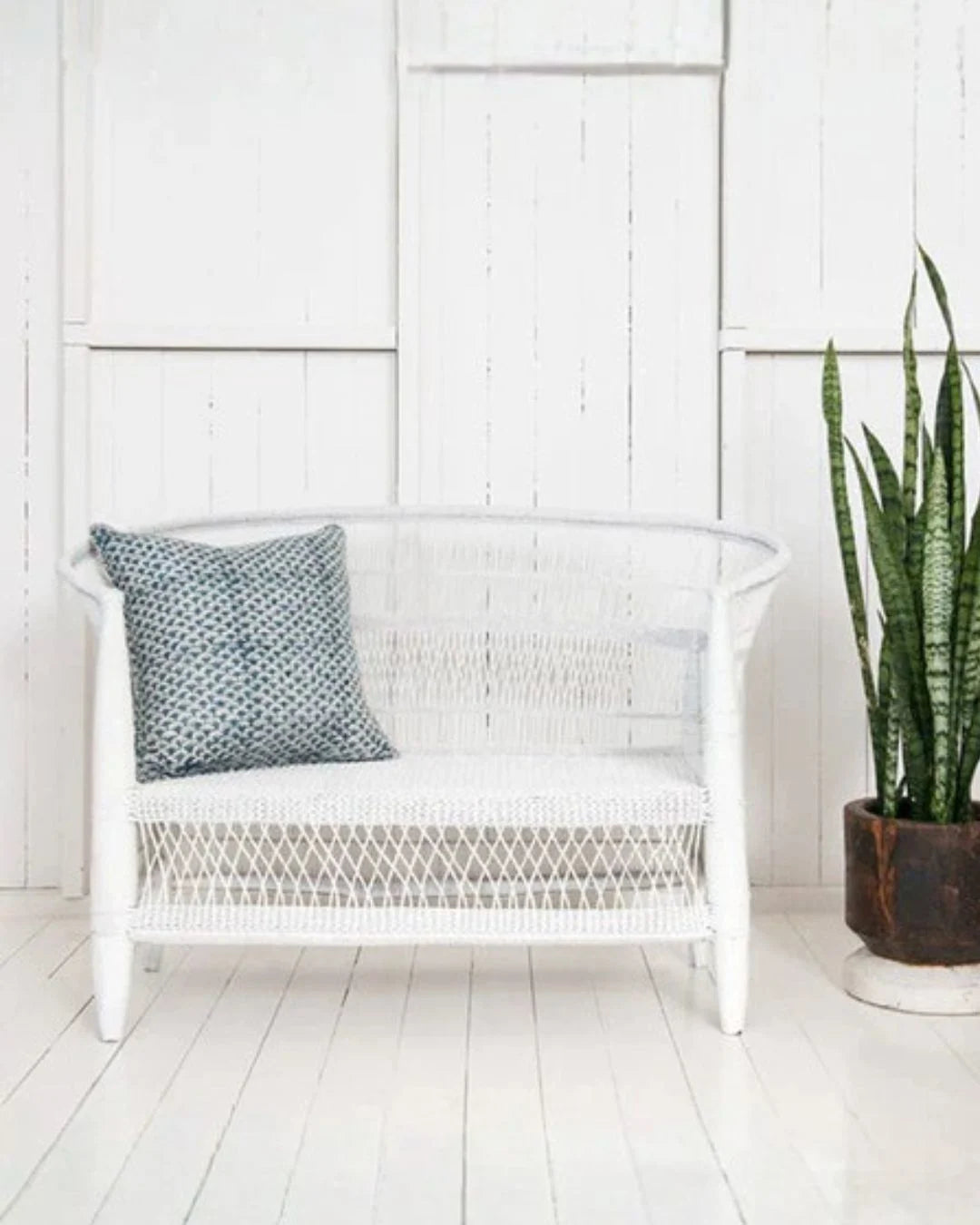White wicker chair with a patterned pillow against a white paneled wall.