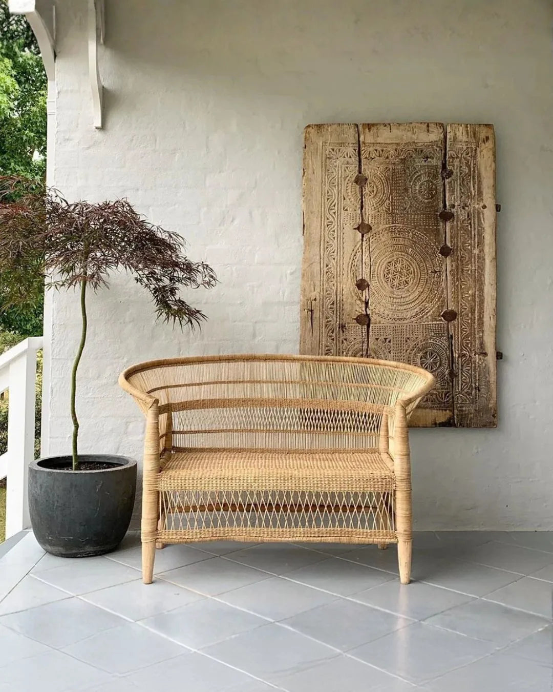 Wicker chair on a patio with a decorative wall panel and potted plant.