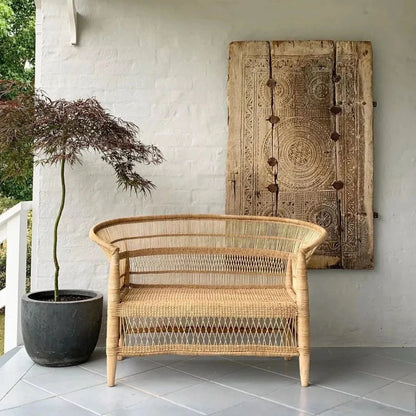 Wicker chair on a patio with a decorative wall panel and potted plant.