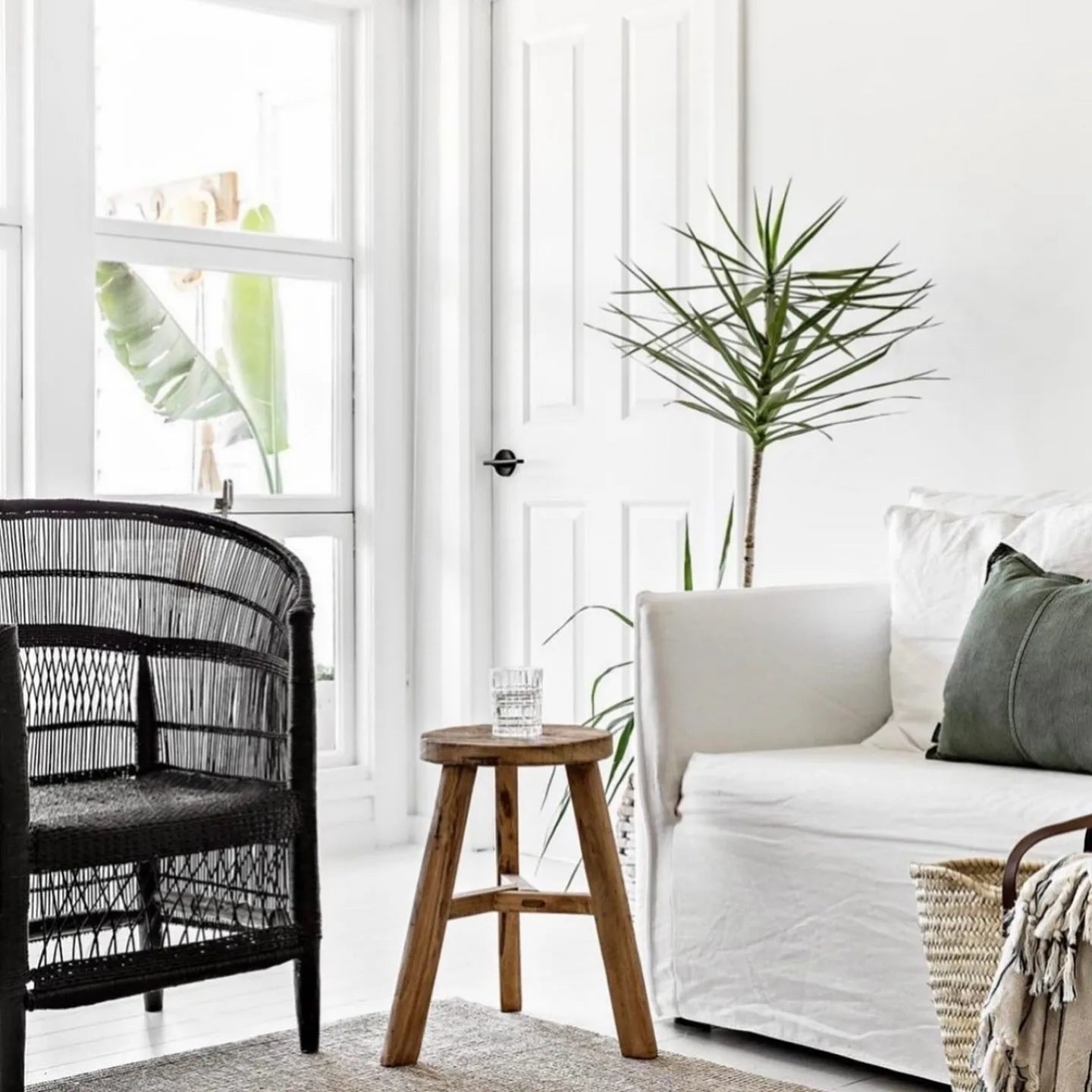 Modern living room with black wicker chair, wooden stool, and white sofa.