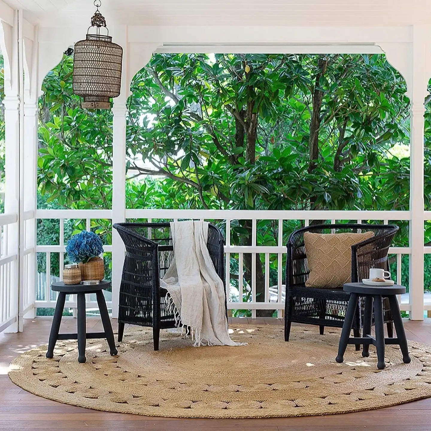Outdoor patio with black Malawi Cane chairs, round rug, and potted plants on a wooden deck.