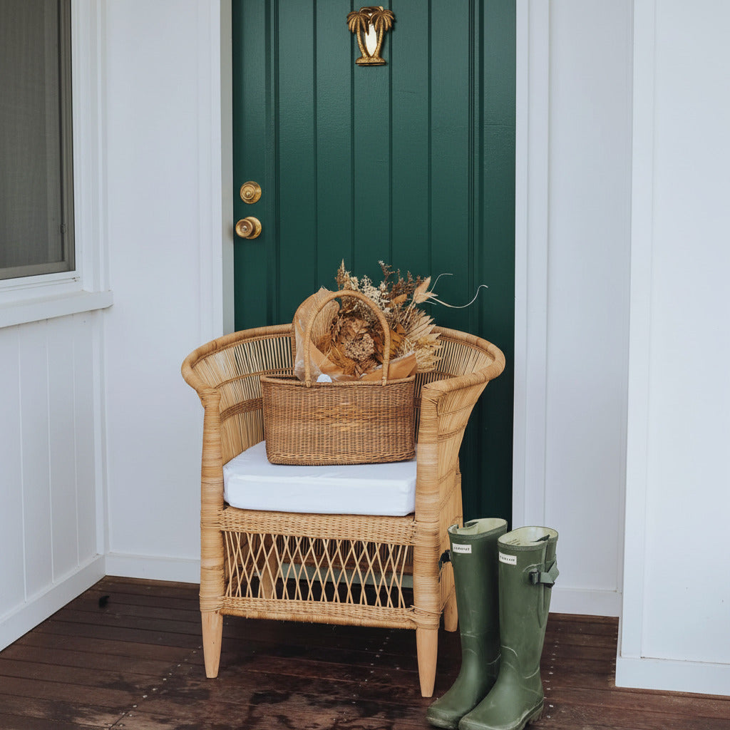 Wicker chair with a cushion and a basket, green boots on a wooden floor against a light blue door.