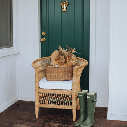 Wicker chair with a cushion and a basket, green boots on a wooden floor against a light blue door.
