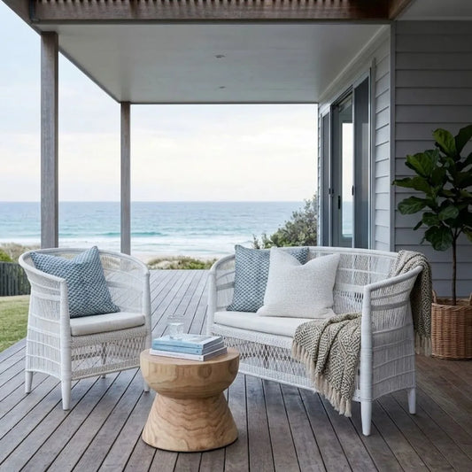 Outdoor seating area with white wicker chairs and a wooden table on a deck overlooking the ocean.