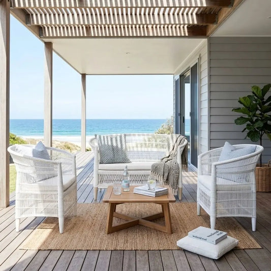 Outdoor patio with white wicker chairs, a wooden coffee table, and ocean view.