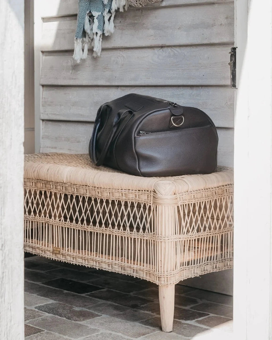 Black leather bag on a wicker bench against a wooden wall.