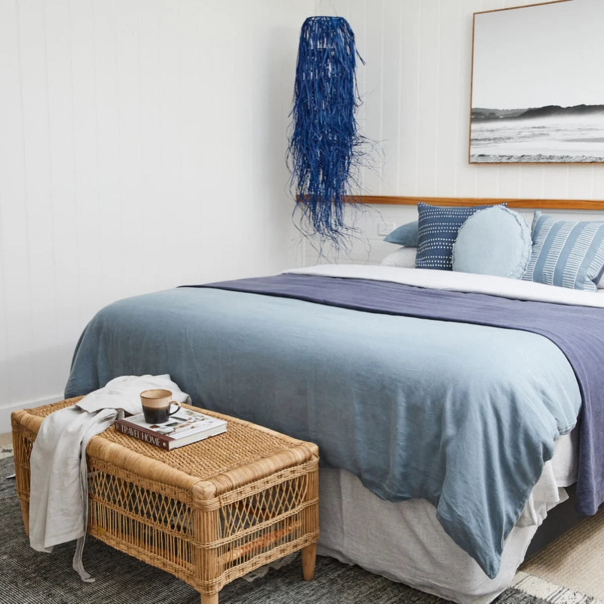Bedroom with a bed featuring blue and purple bedding, a woven ottoman, and decorative items.