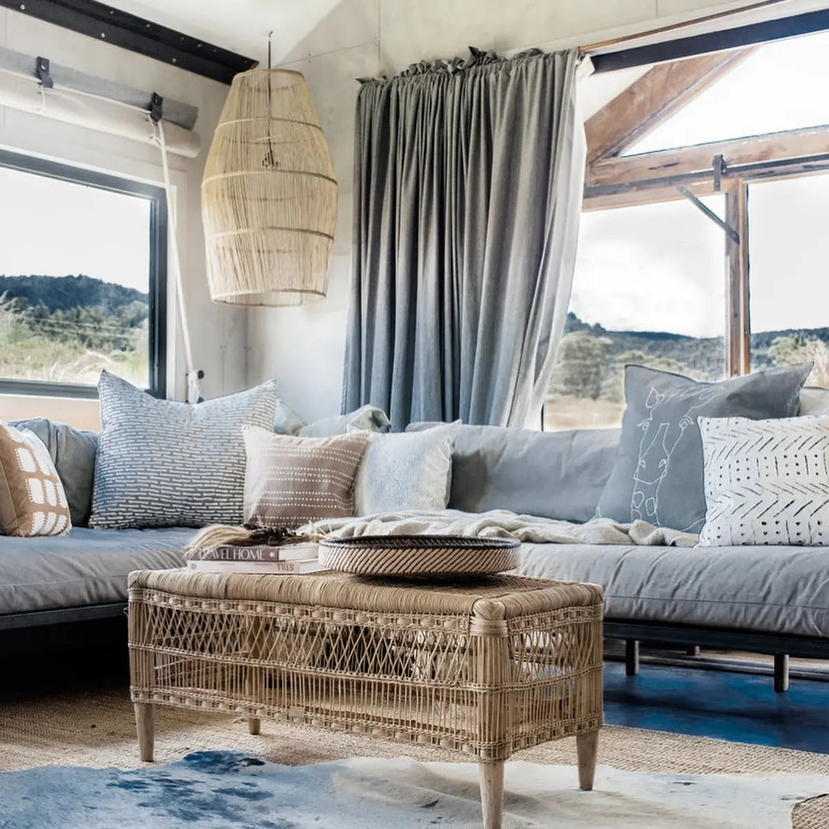 Living room with a gray sectional sofa, wicker coffee table, and large windows.