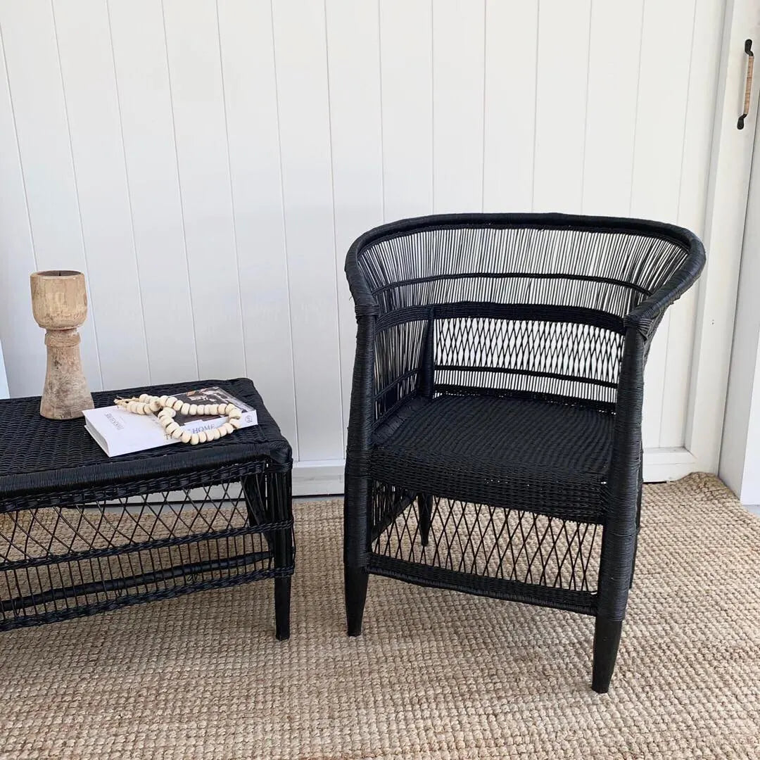 Black wicker chair and side table against a white paneled wall.