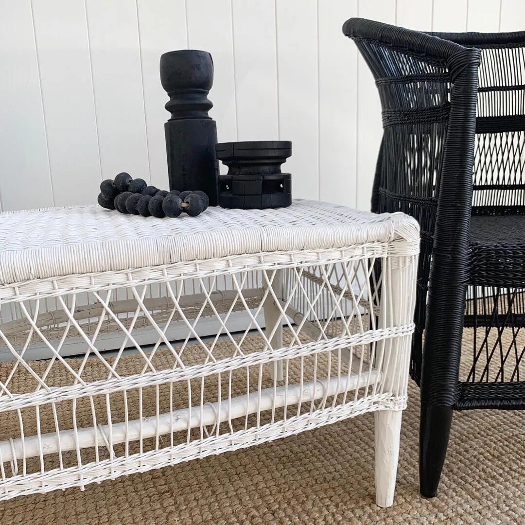 White wicker bench with black decorative items against a white wall.