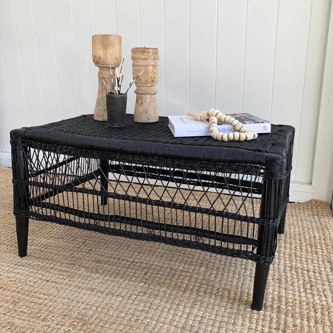 Black wicker coffee table with decorative items on a beige carpet