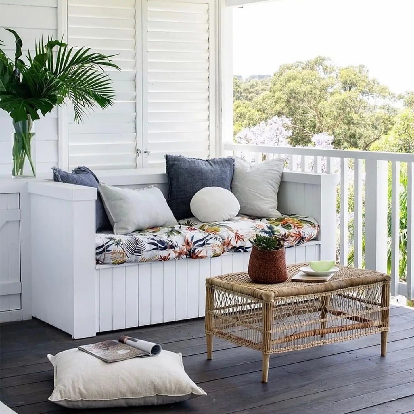 Outdoor seating area with a white bench, cushions, and a woven table on a wooden deck.