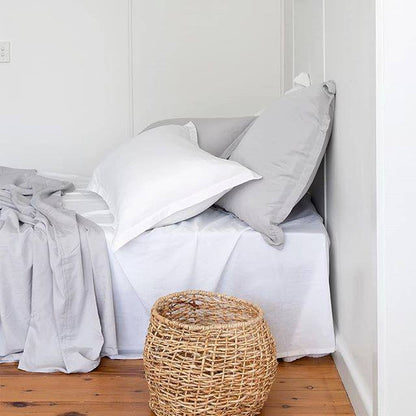 Bed with white and gray pillows and a woven stool in a bedroom.