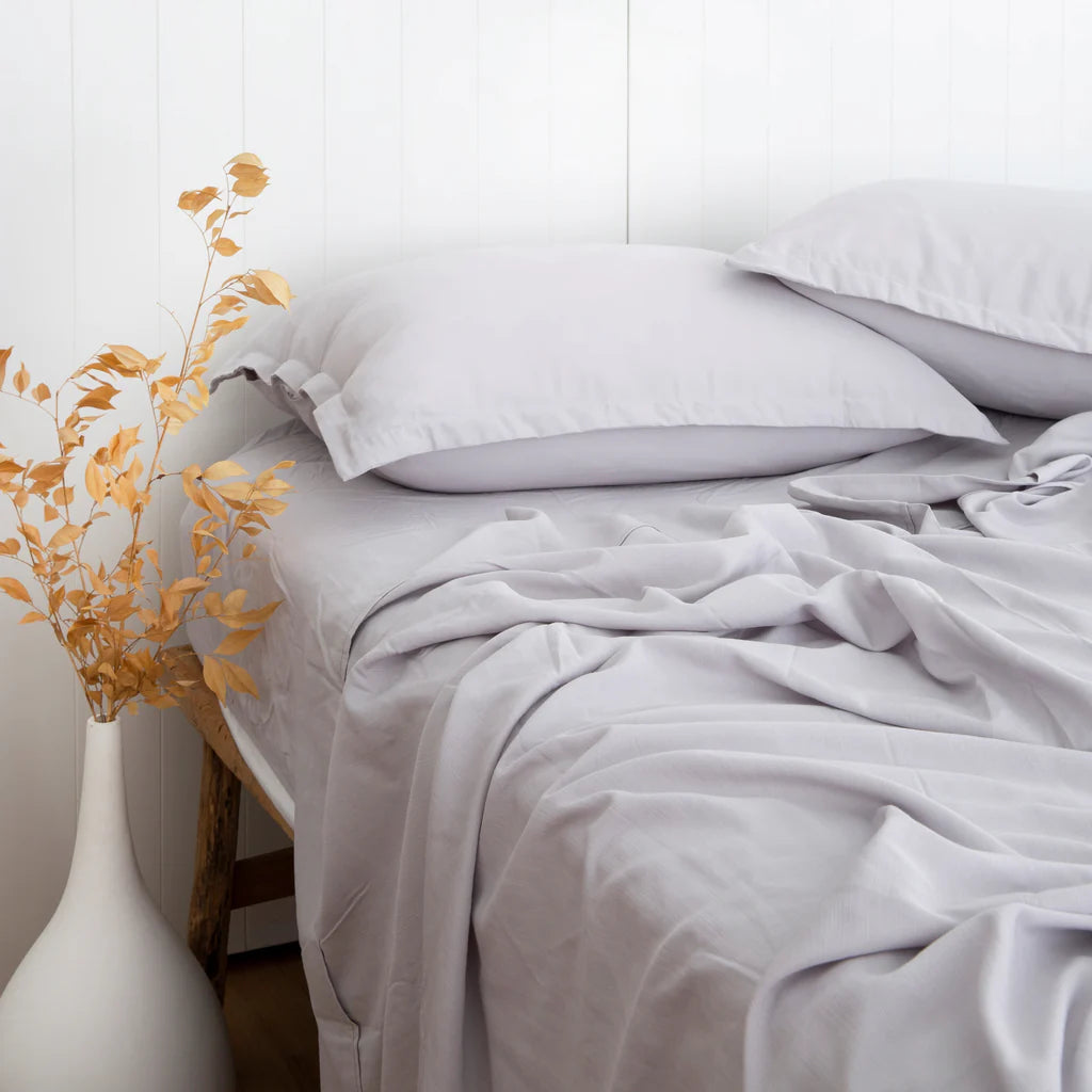 Neatly made bed with white bedding and a vase with yellow leaves on a white background