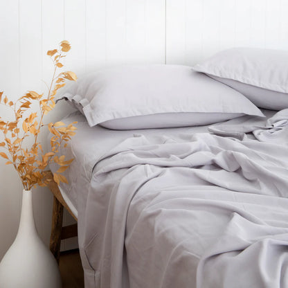 Neatly made bed with white bedding and a vase with yellow leaves on a white background