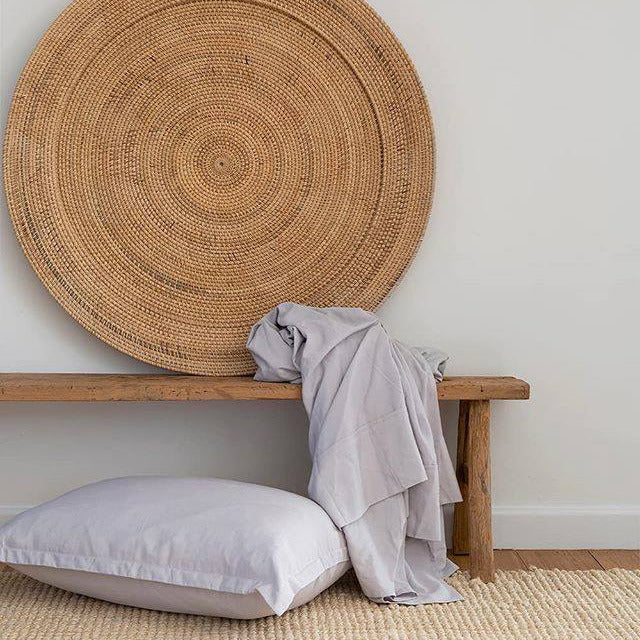 Woven headboard on a wall with a wooden bench, pillow, and blanket in a neutral room.