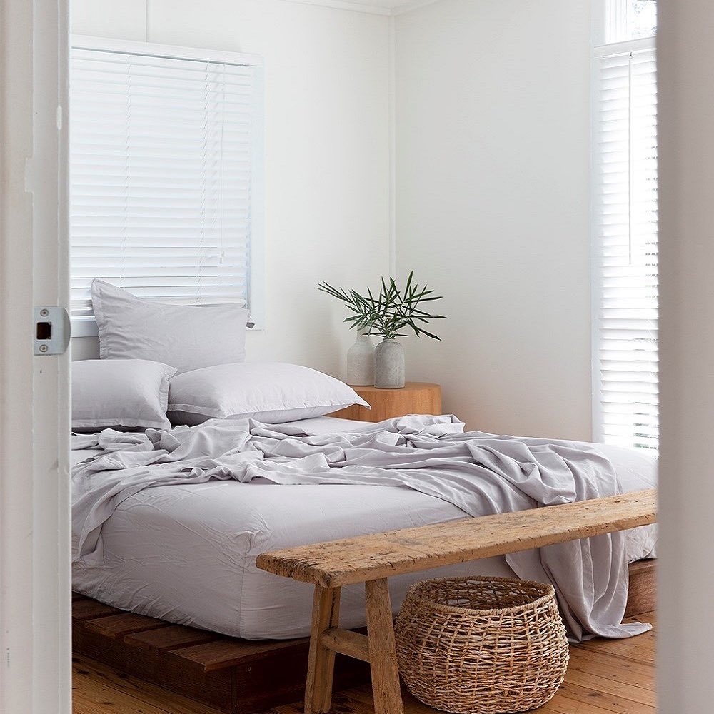 Neatly made bed with white bedding and a wooden bench in a bright bedroom.