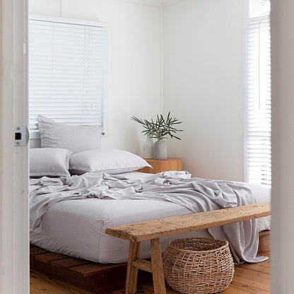 Neatly made bed with white bedding and a wooden bench in a bright bedroom.