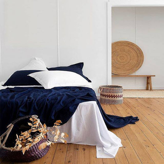 Bed with navy and white bedding in a room with wooden flooring and a woven basket.