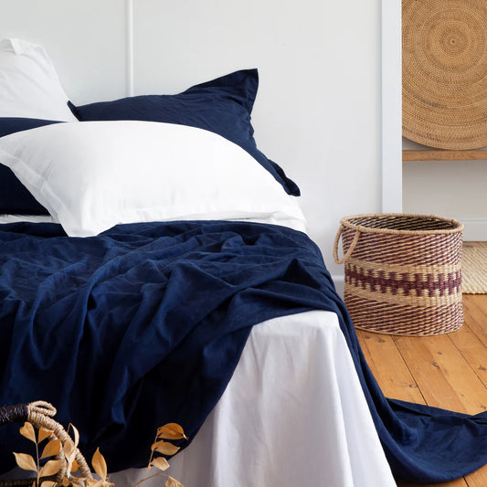 Navy blue and white bedding on a bed with a woven basket in the background.