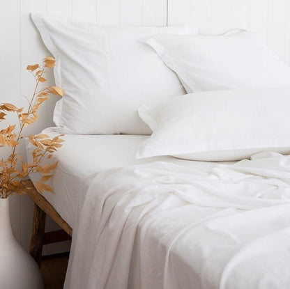 White bedding set on a bed with a vase of flowers on a white background