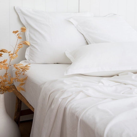 White bedding set on a bed with a vase of flowers on a white background