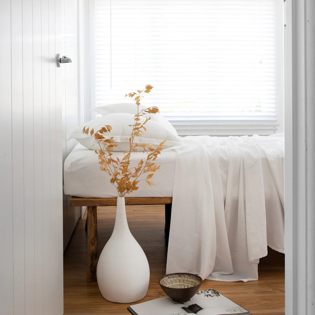White vase with gold leaves on a wooden stool in a room with white walls and a window.