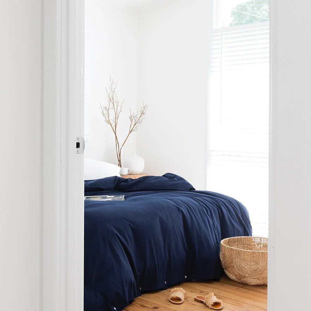 Navy blue duvet cover on a bed in a bright bedroom with white walls and wooden floor.
