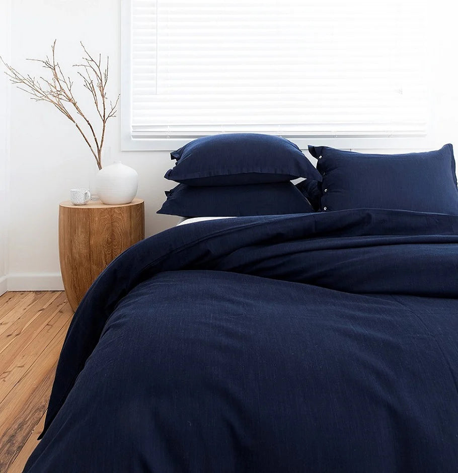 Navy blue bedding set on a bed in a room with a wooden side table and plant.
