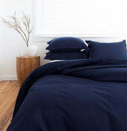 Navy blue bedding set on a bed in a room with a wooden side table and plant.