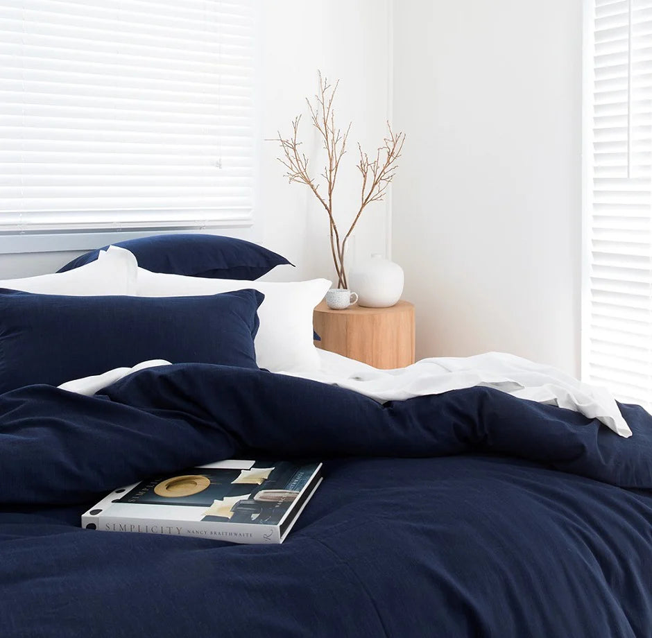 Navy blue bedding set on a bed with a white pillow and a small wooden side table with decorative items.