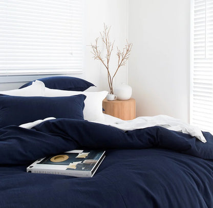Navy blue bedding set on a bed with a white pillow and a small wooden side table with decorative items.
