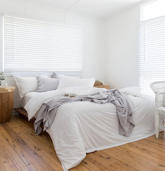 Neatly made bed with white bedding and gray throw blanket in a bright bedroom.