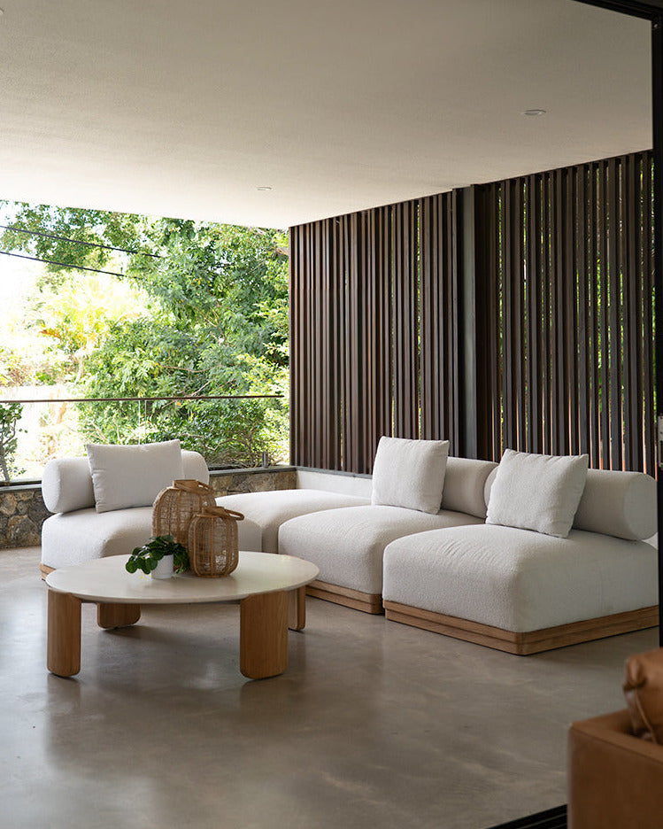 Modern outdoor living space with white sofa, wooden coffee table, and large windows.