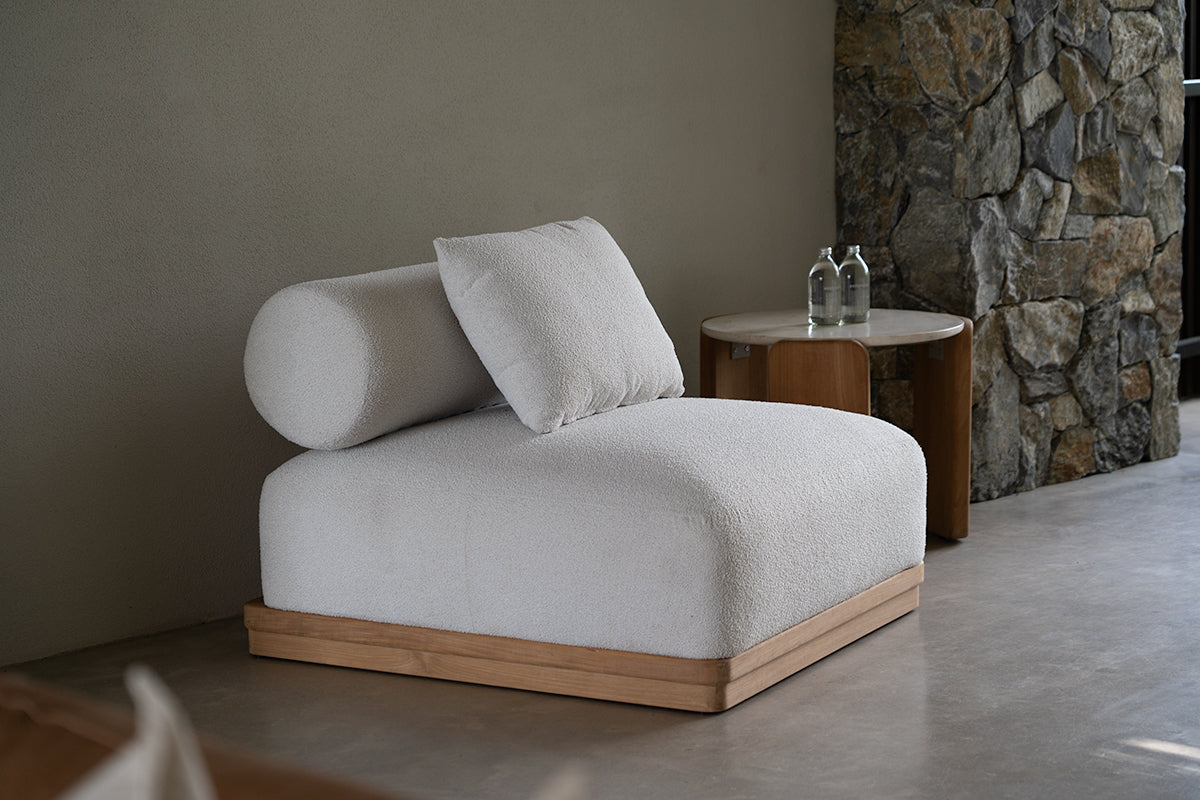 Modern white Baska chair a with wooden base in a room with stone wall and small table.