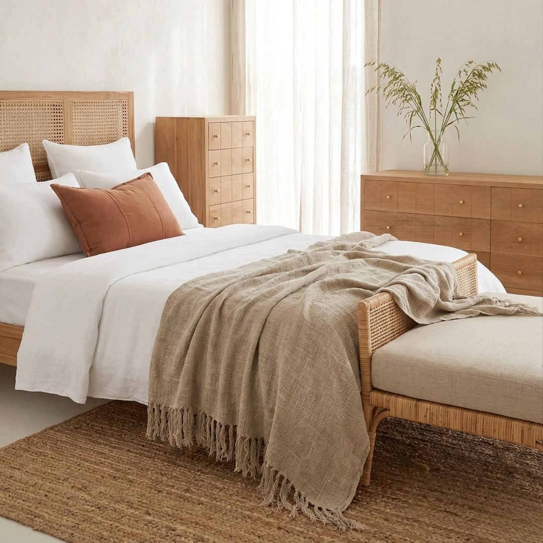 Bedroom with wooden furniture, bed with white bedding and brown blanket, and a vase with plants on a dresser.