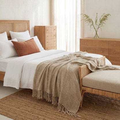 Bedroom with wooden furniture, bed with white bedding and brown blanket, and a vase with plants on a dresser.