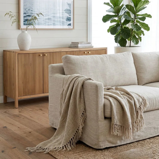 Beige sofa with a blanket draped over it in a living room setting.